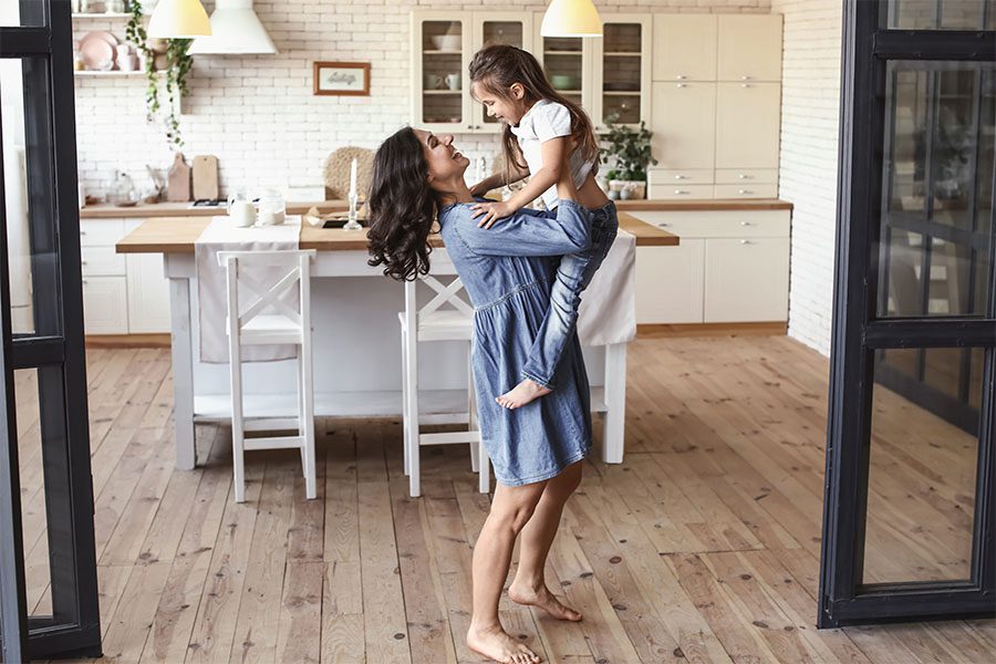 Personal Insurance - Portrait of a Happy Mother Holding Up Her Daughter While Standing in the Kitchen at Home