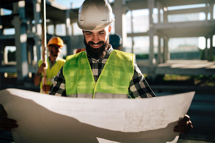 Specialized Business Insurance - Portrait of a Smiling Male Contractor Holding Up New Building Blue Prints While Standing on a Construction Jobsite